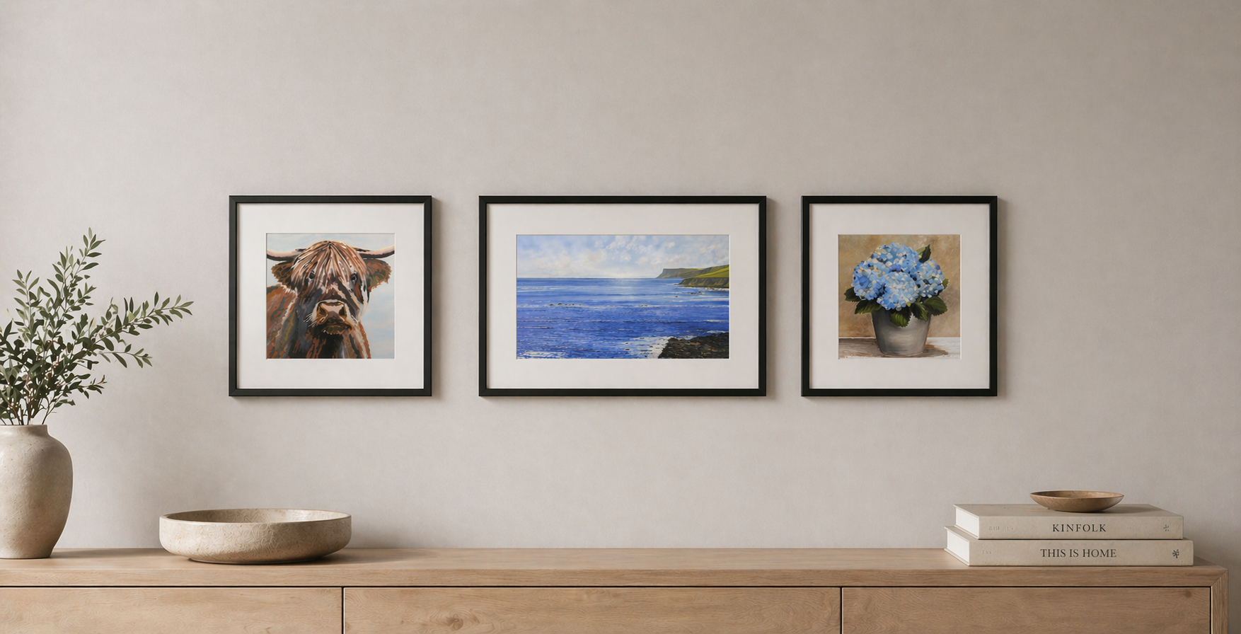 Three framed artworks on a wall above a wooden cabinet.